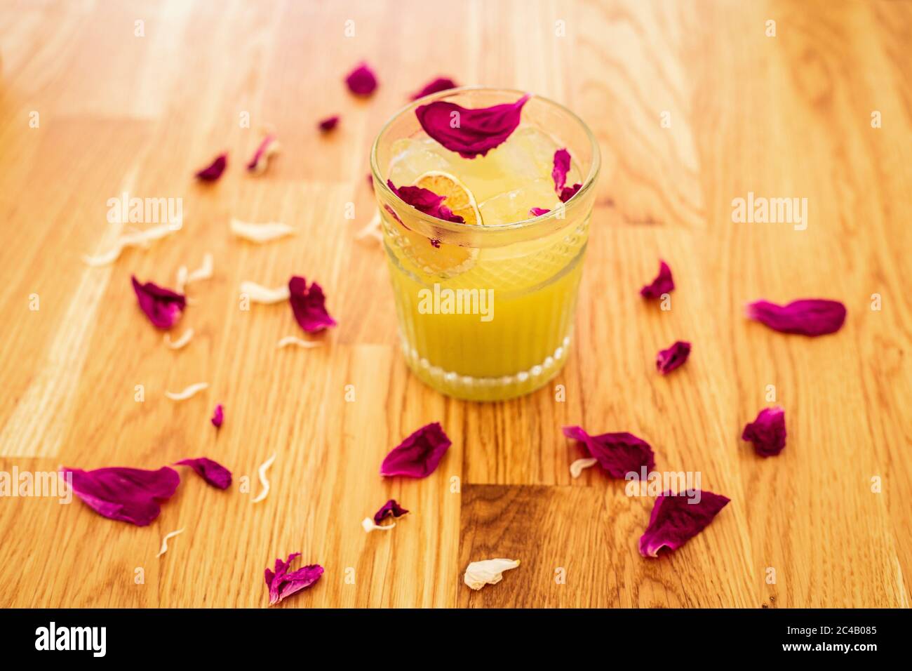 Ein erfrischender Zitruscocktail mit Eis in einem Steinglas, das mit einer trockenen Orangenscheibe und Rosenblättern verziert ist Stockfoto