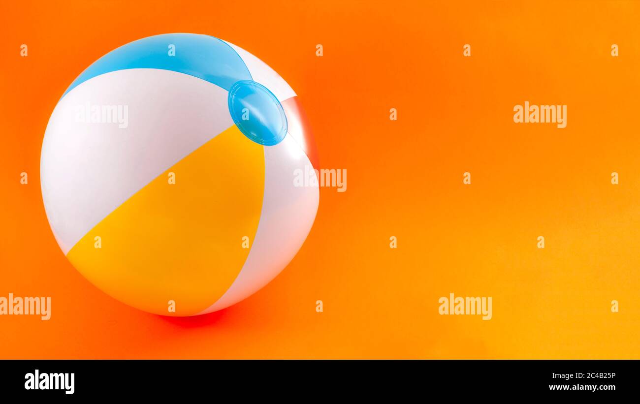 Sommerurlaub, Strandspielzeug und Badespaß-Aktivitäten-Konzept mit einem aufblasbaren Strandball isoliert auf orangenen Hintergrund mit Kopierraum Stockfoto