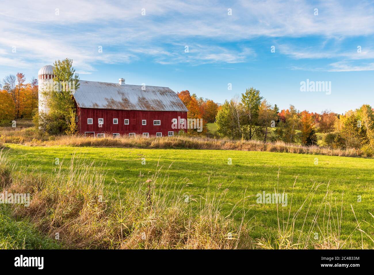Idyllische ländliche Landschaft unter blauem Himmel mit einer alten roten Holzscheune mit Silo am Ende eines Grasfeldes am sonnigen Herbsttag Stockfoto