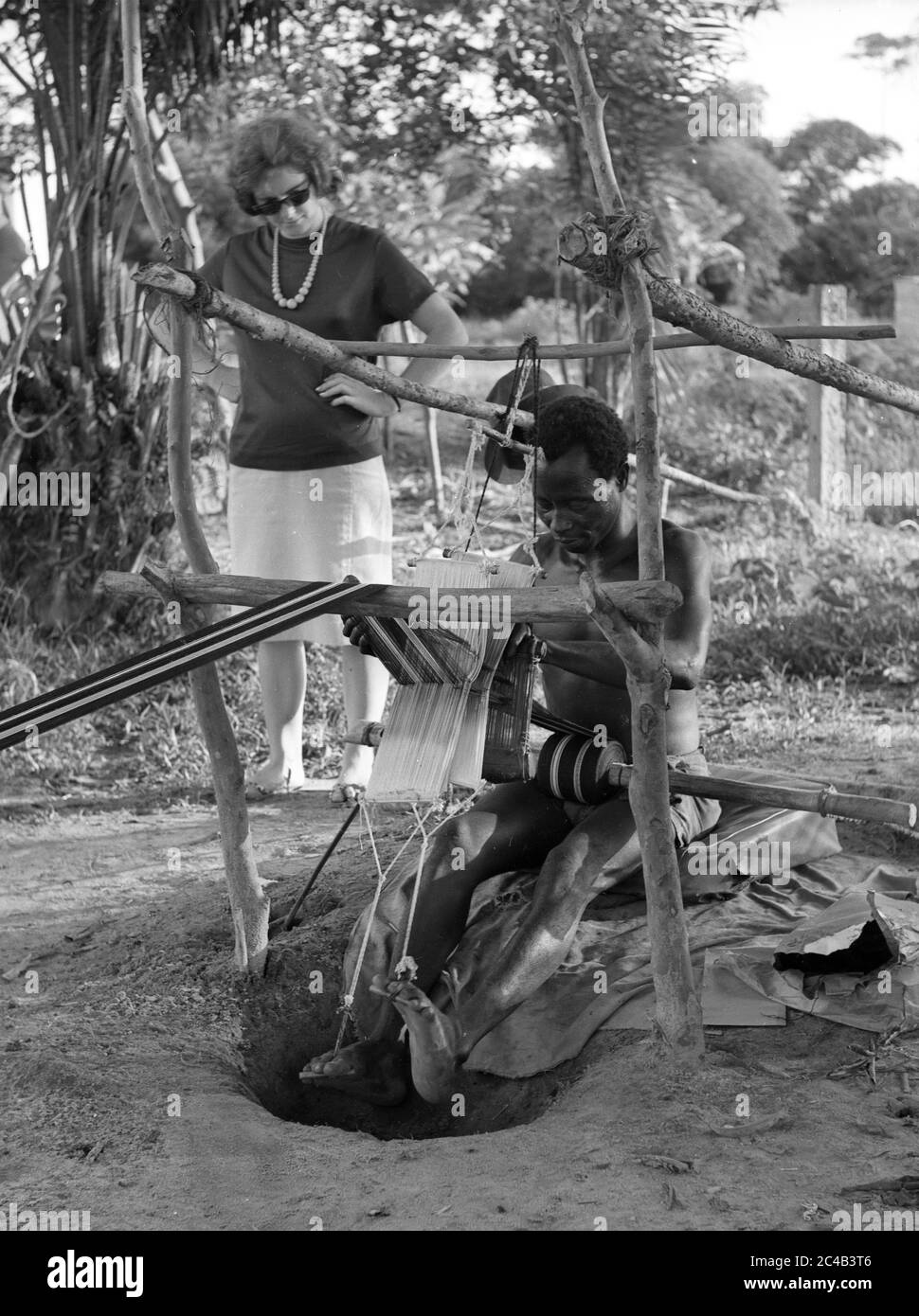 Elfenbeinküste 1963 westliche Touristen beobachten westafrikanischen Mann, der einen Tretwebstuhl betätigt Stockfoto