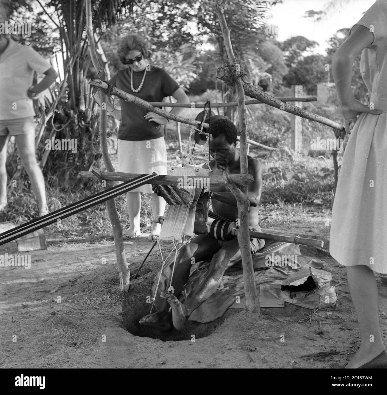Elfenbeinküste 1963 westliche Touristen beobachten westafrikanischen Mann, der einen Tretwebstuhl betätigt Stockfoto