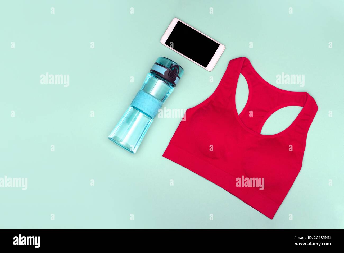 Das Konzept des Home Workouts. Sporttop, Wasserflasche, Telefon auf türkisfarbenem Hintergrund. Flach liegend. Stockfoto