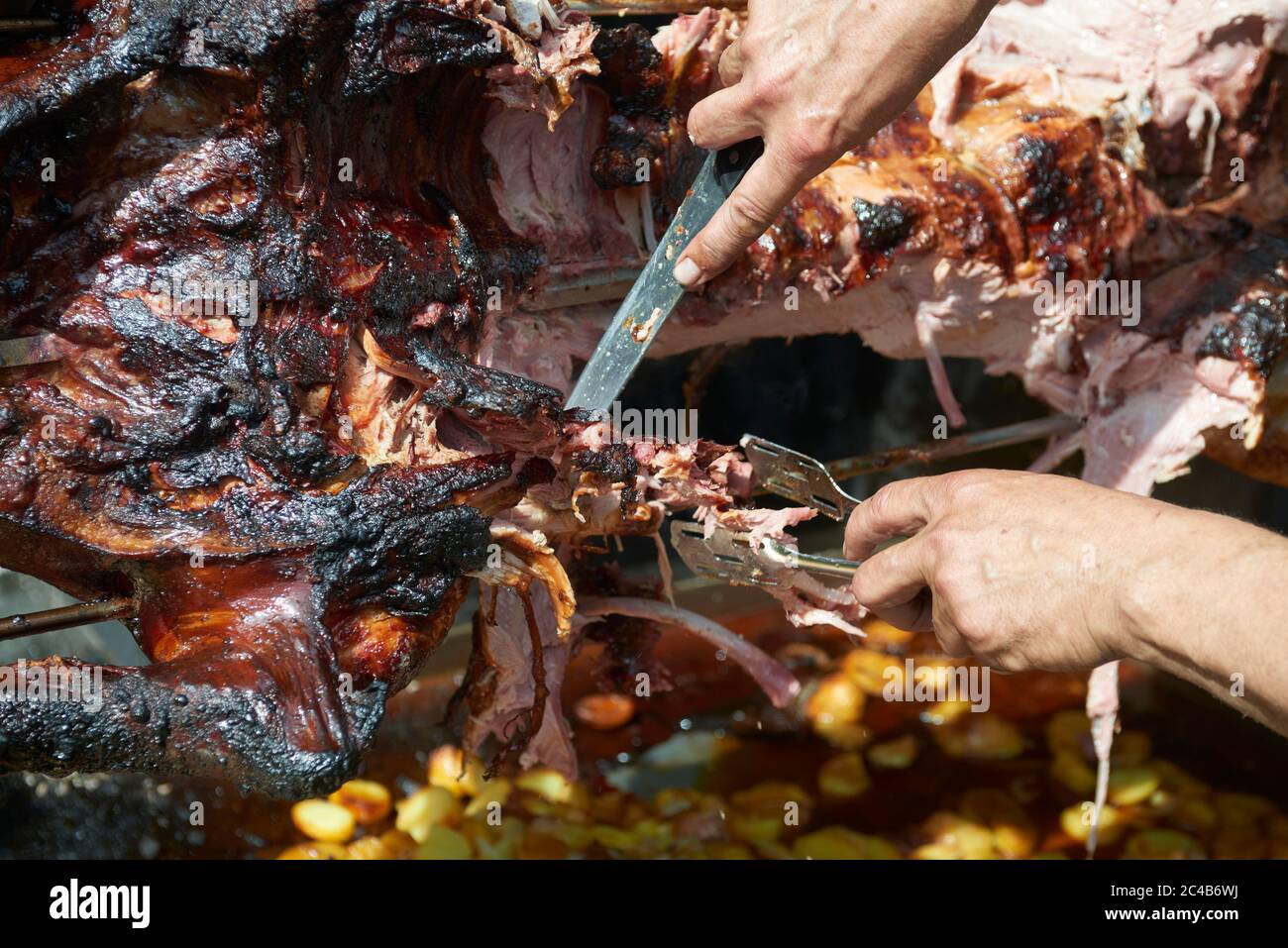 Chef Hände Schneiden ganze gegrillte Schweinefleisch für Steaks mit Messer. Vom Schwein gegrillte traditionelle Kohle und Feuer. Das kleine Schwein wird ganz auf einem offenen Feuer geröstet. Stockfoto