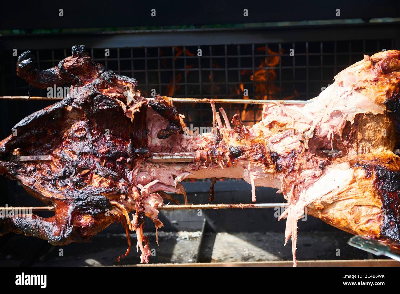 Chef Hände Schneiden ganze gegrillte Schweinefleisch für Steaks mit Messer. Vom Schwein gegrillte traditionelle Kohle und Feuer. Das kleine Schwein wird ganz auf einem offenen Feuer geröstet. Stockfoto