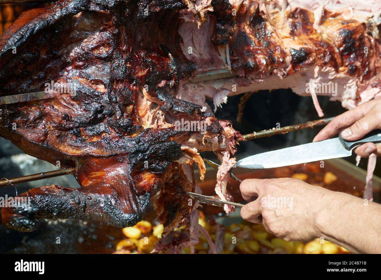 Chef Hände Schneiden ganze gegrillte Schweinefleisch für Steaks mit Messer. Vom Schwein gegrillte traditionelle Kohle und Feuer. Das kleine Schwein wird ganz auf einem offenen Feuer geröstet. Stockfoto