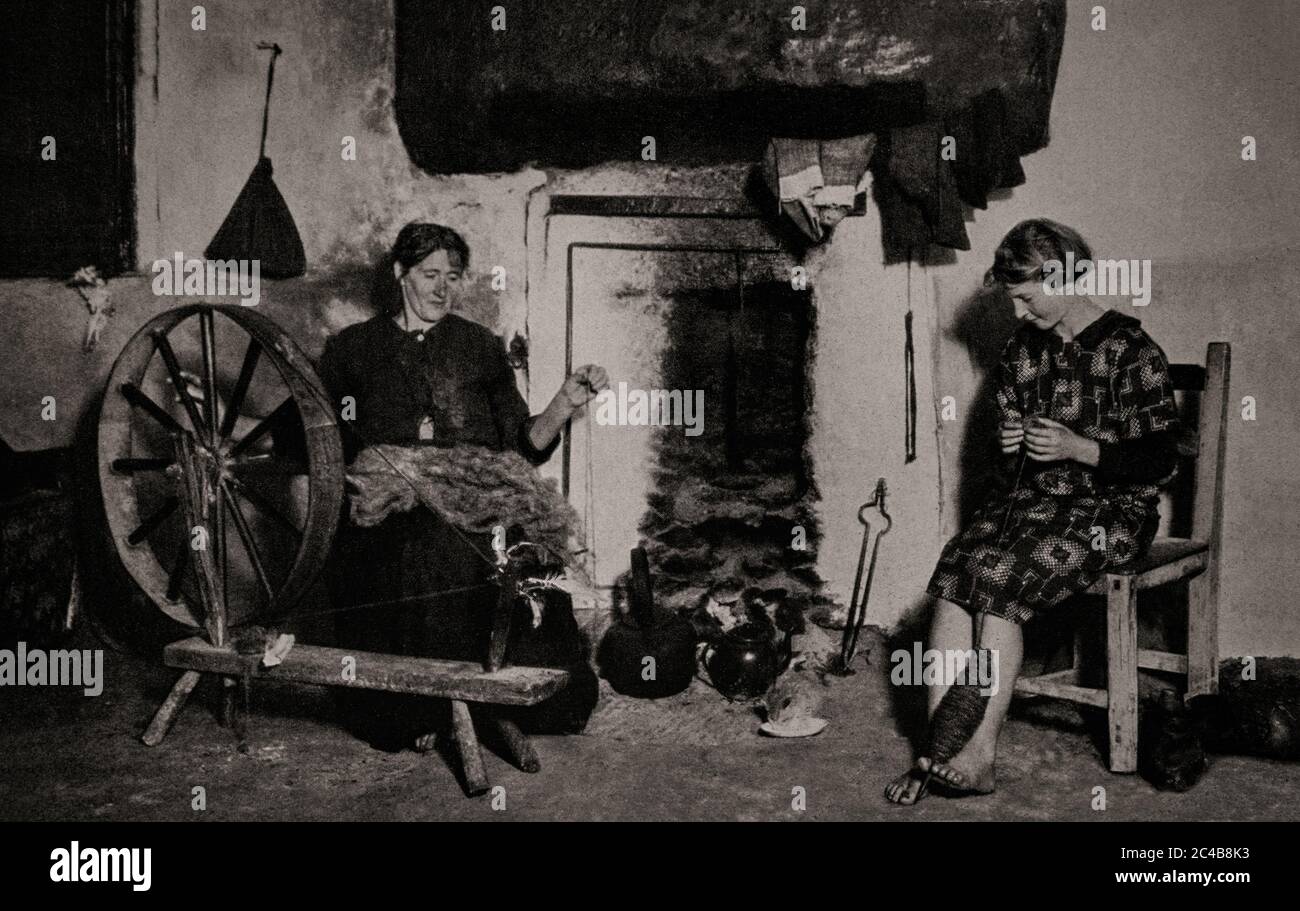 Eine Szene des ländlichen irischen Lebens in den frühen 1920er Jahren in der Nähe von Smerwick Harbour, Grafschaft Kerry. Die ältere Dame (links) spinnt Wolle zu Garn, während die jüngere Frau die Spindel des Garns zwischen ihren Zehen hält, damit sie das Garn zu einer Kugel aufwickeln kann. Ursprünglich fotografiert von Clifton Adams (1890-1934) für 'Ireland: The Rock Whence I Was Hewn', eine National Geographic Magazine-Spielfilm vom März 1927. Stockfoto