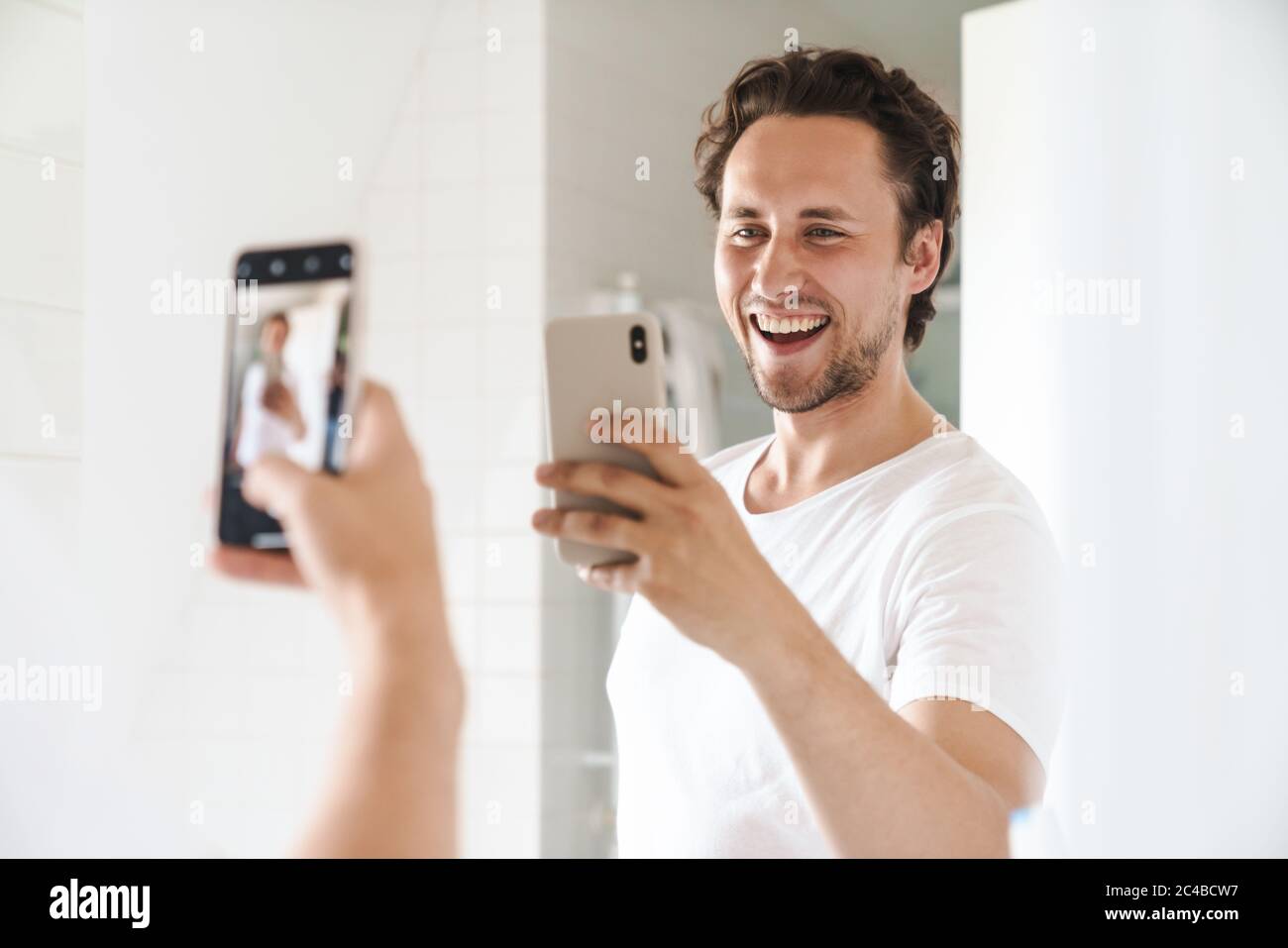 Attraktiver, glücklicher junger Mann, der vor dem Badezimmerspiegel steht und ein Selfie macht Stockfoto