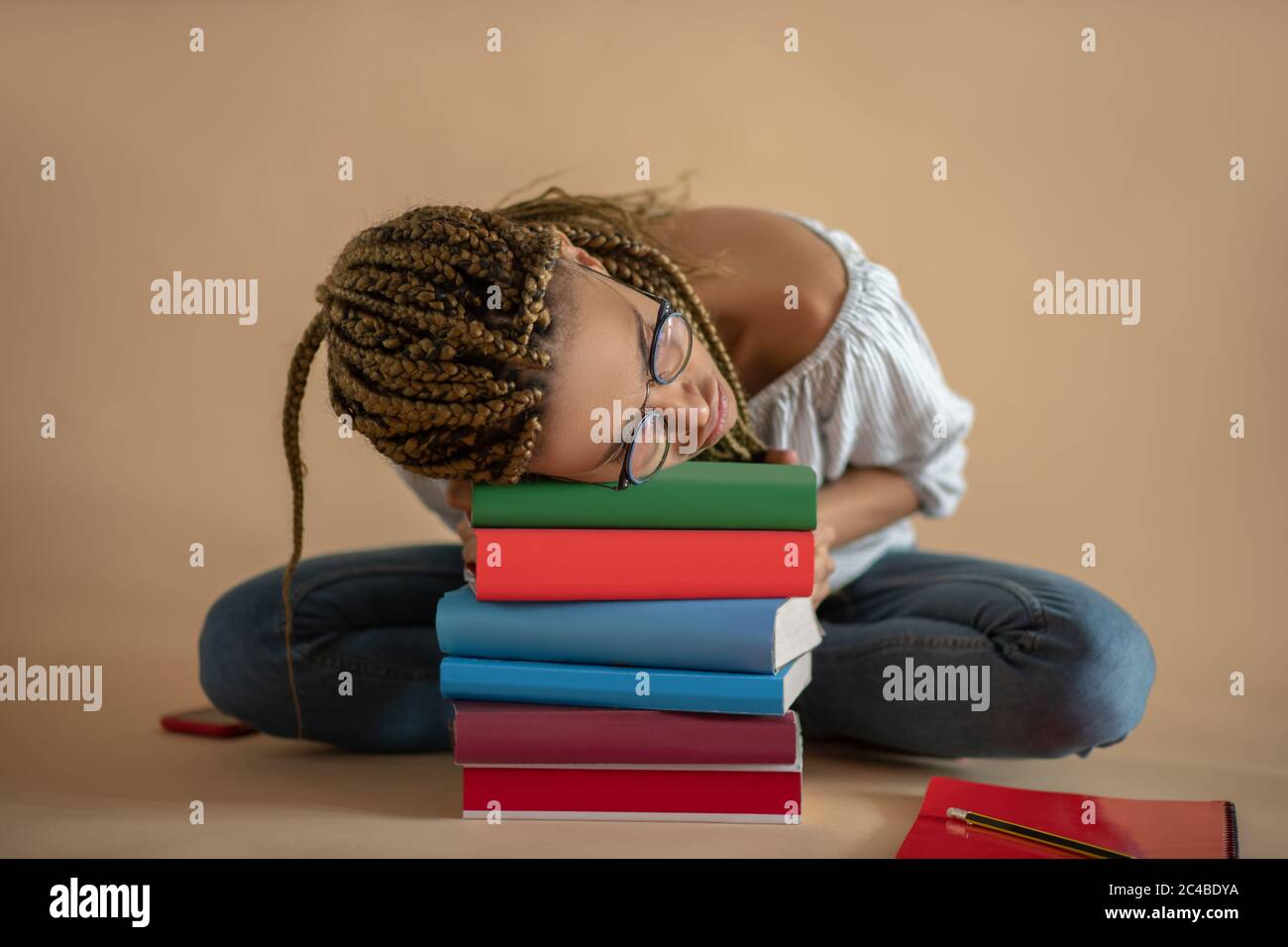 Müde junge afroamerikanische Frau in Brillen schlafen auf Haufen von Büchern Stockfoto