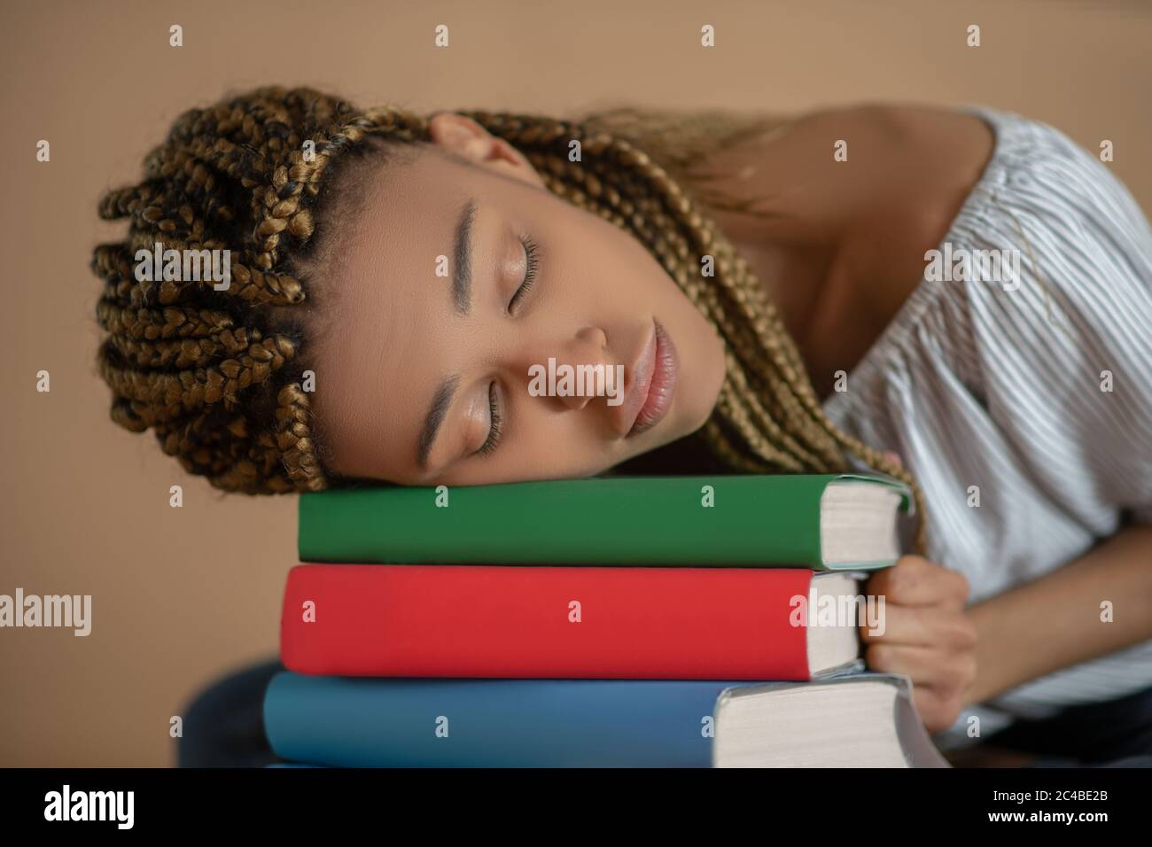 Müde junge afroamerikanische Frau schlafen auf Haufen von Büchern Stockfoto