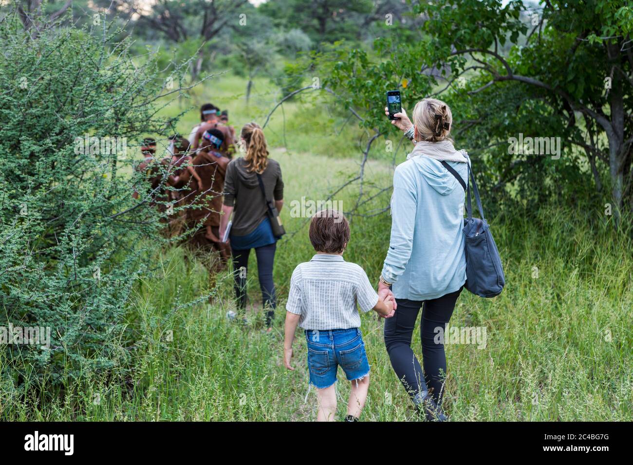 Ein Junge und seine Mutter, Touristen auf einem Wanderweg, die Mitglieder der San, Buschmänner folgen. Stockfoto