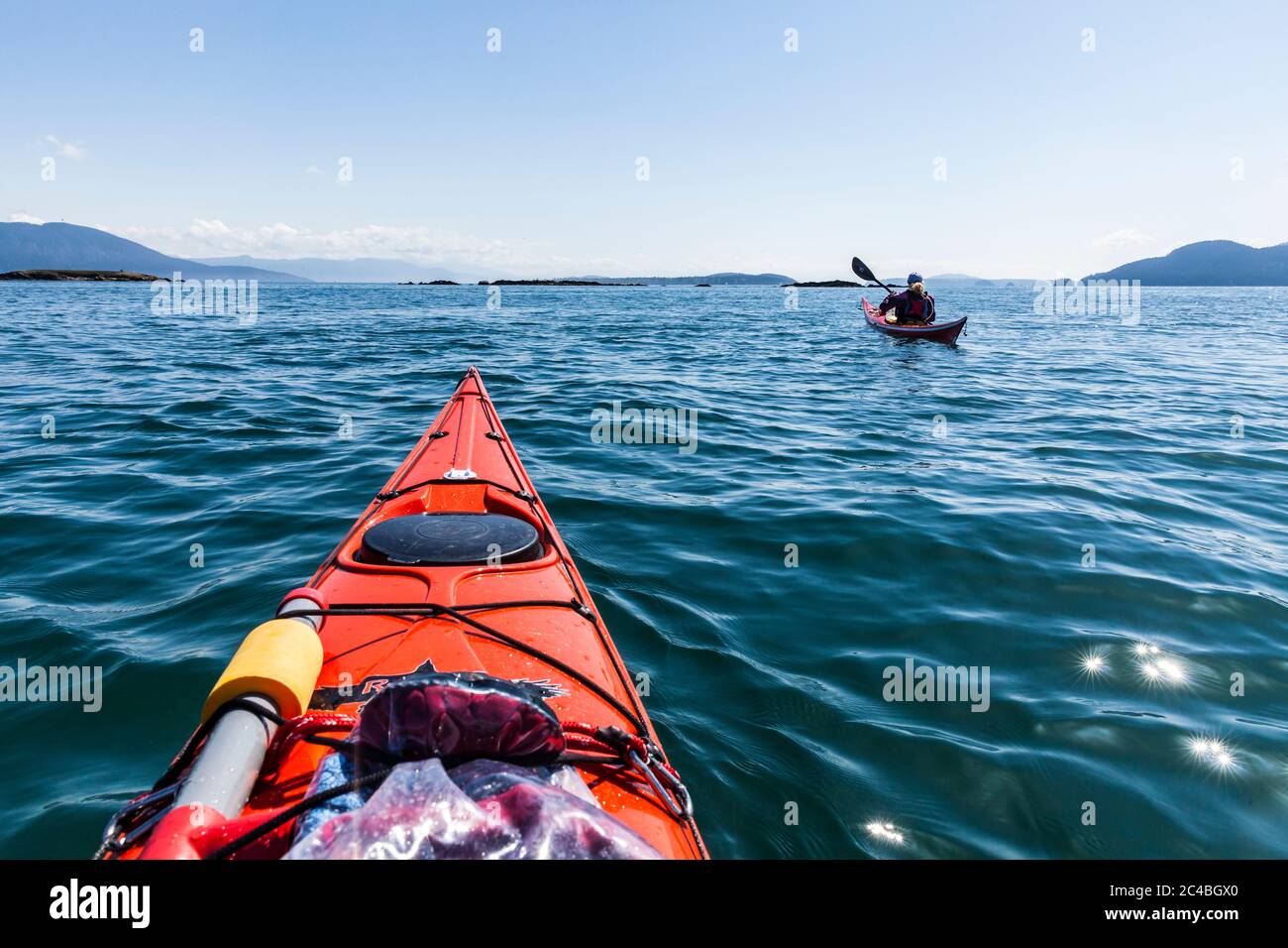 Eine Frau in ihrem Seekajak vor der Südostküste der Orcas Island in der Nähe von Doe Bay, mit den Peapod Rocks im Hintergrund, Washington State, USA. Stockfoto