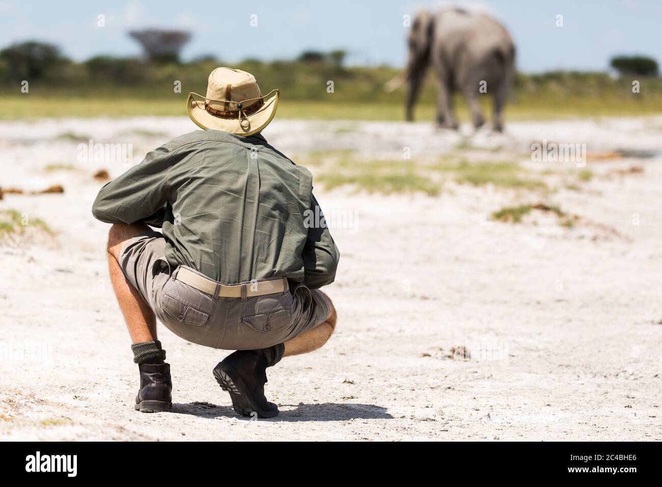 Ein Führer, der in der Nähe eines Elefanten in Nxai Pan, Botswana hockend Stockfoto