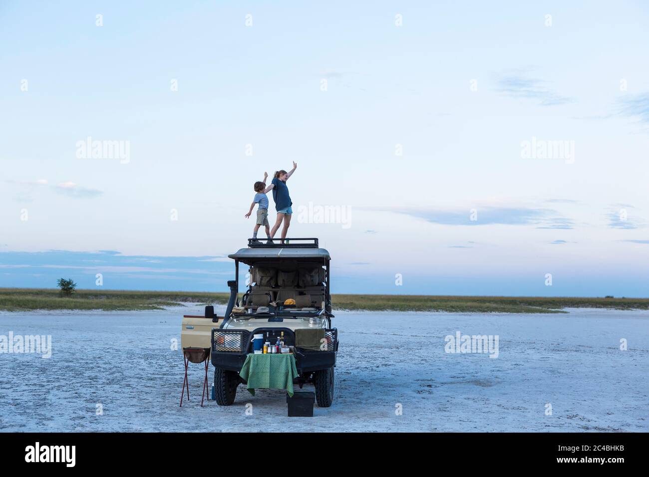 Ein Bruder und eine Schwester stehen in der Abenddämmerung auf einem Safarizeps in einer Salzpfannenlandschaft Stockfoto