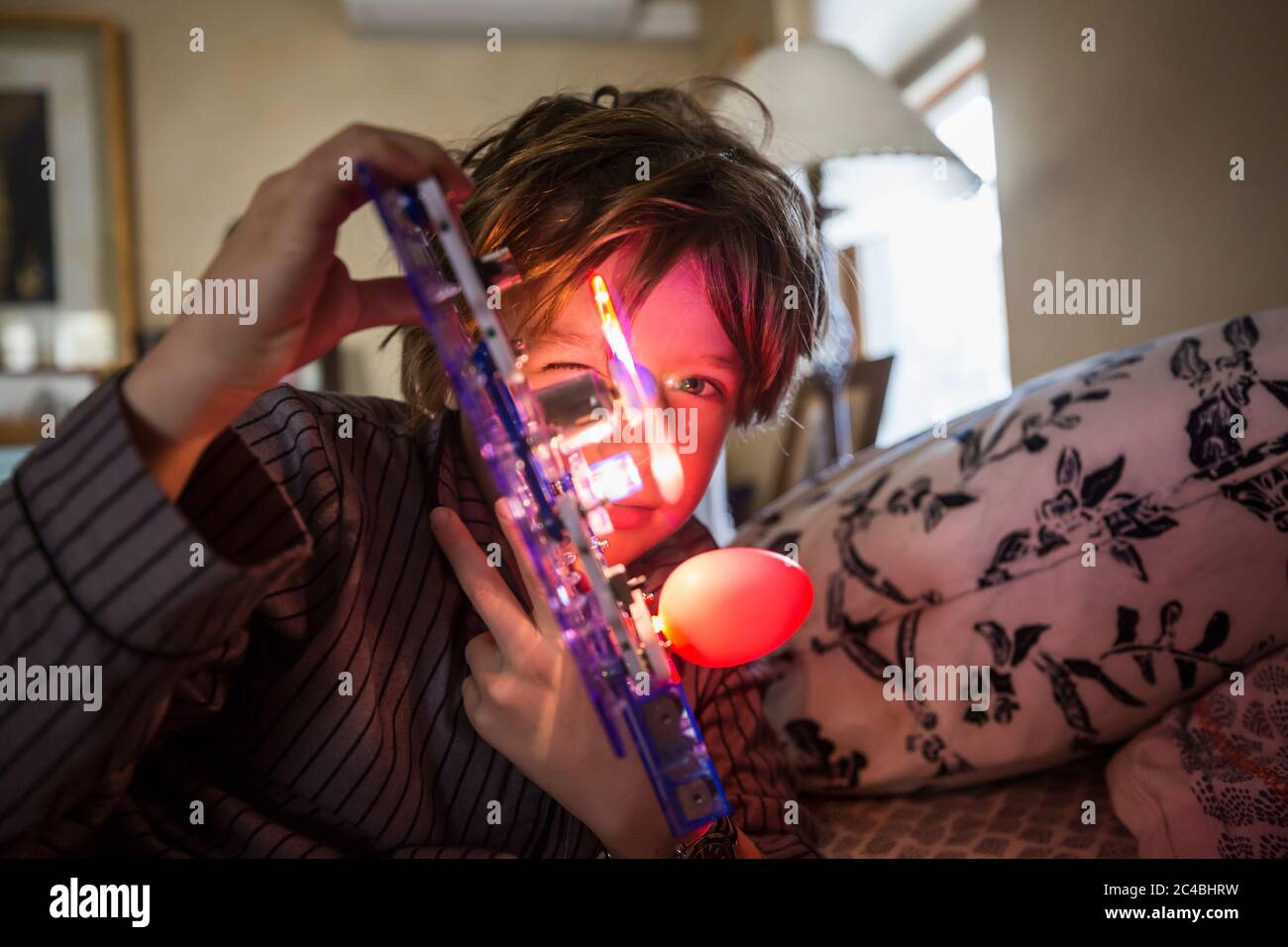 Ein sechsjähriger Junge, der bei schwachem Licht mit einem beleuchteten Spielzeug zu Hause spielt. Stockfoto