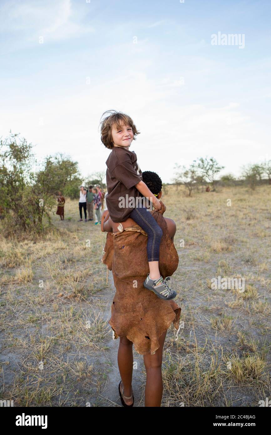 Fünfjähriger Junge, der auf den Schultern eines San-Buschmanns reitet. Stockfoto