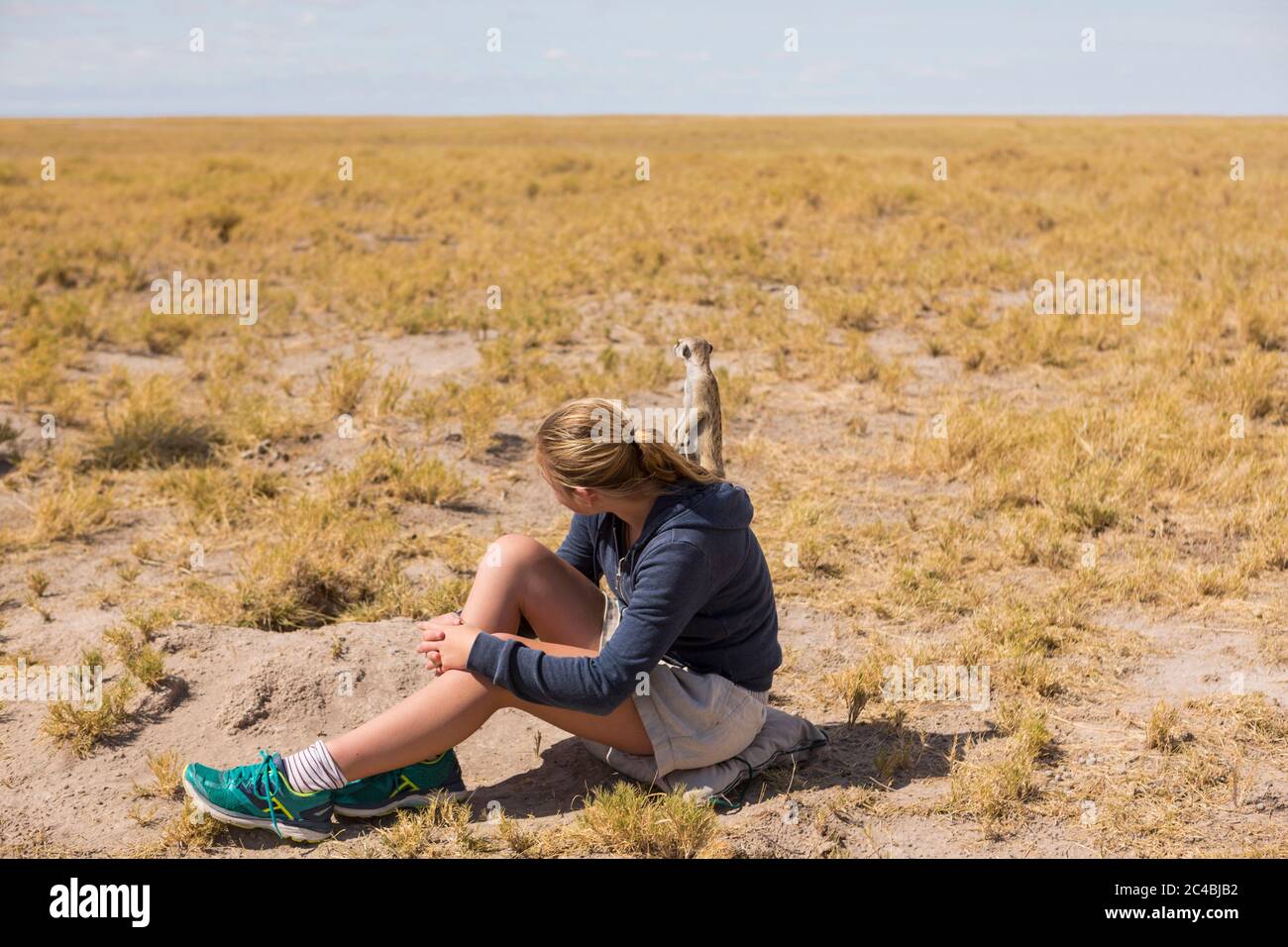 12-jähriges Mädchen, das in der Kalahari-Wüste sitzt und Erdmännchen aus ihren Höhlen auftaucht. Stockfoto