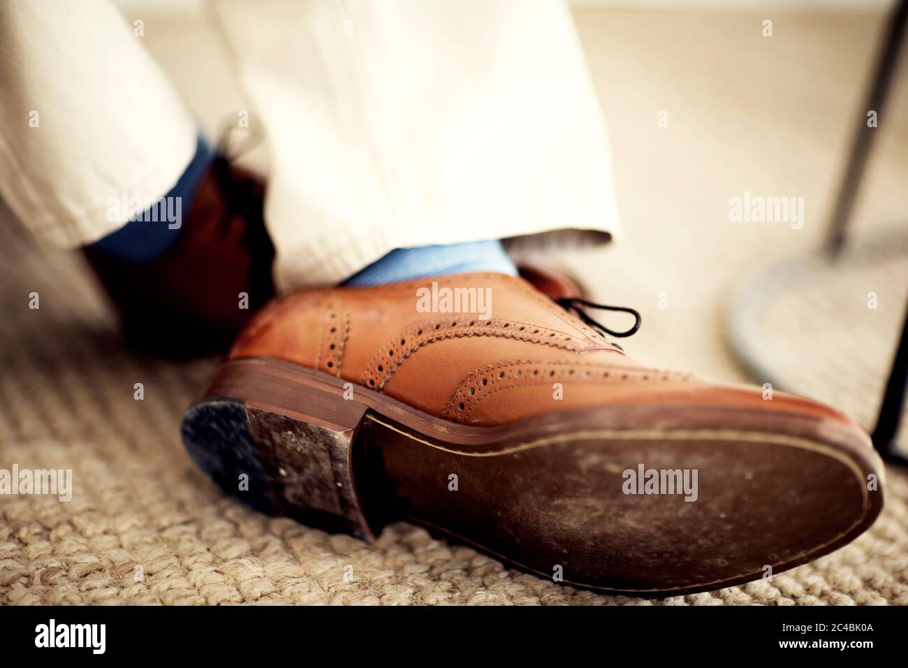 Nahaufnahme der Füße der Person, mit braunen Lederbrogues, blauen Socken und weißen Hosen. Stockfoto