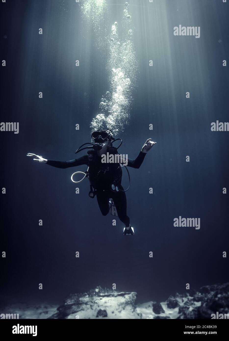 Unterwasseransicht des Tauchers mit Neoprenanzug, Taucherbrille und Sauerstoffflasche, aufsteigende Luftblasen. Stockfoto