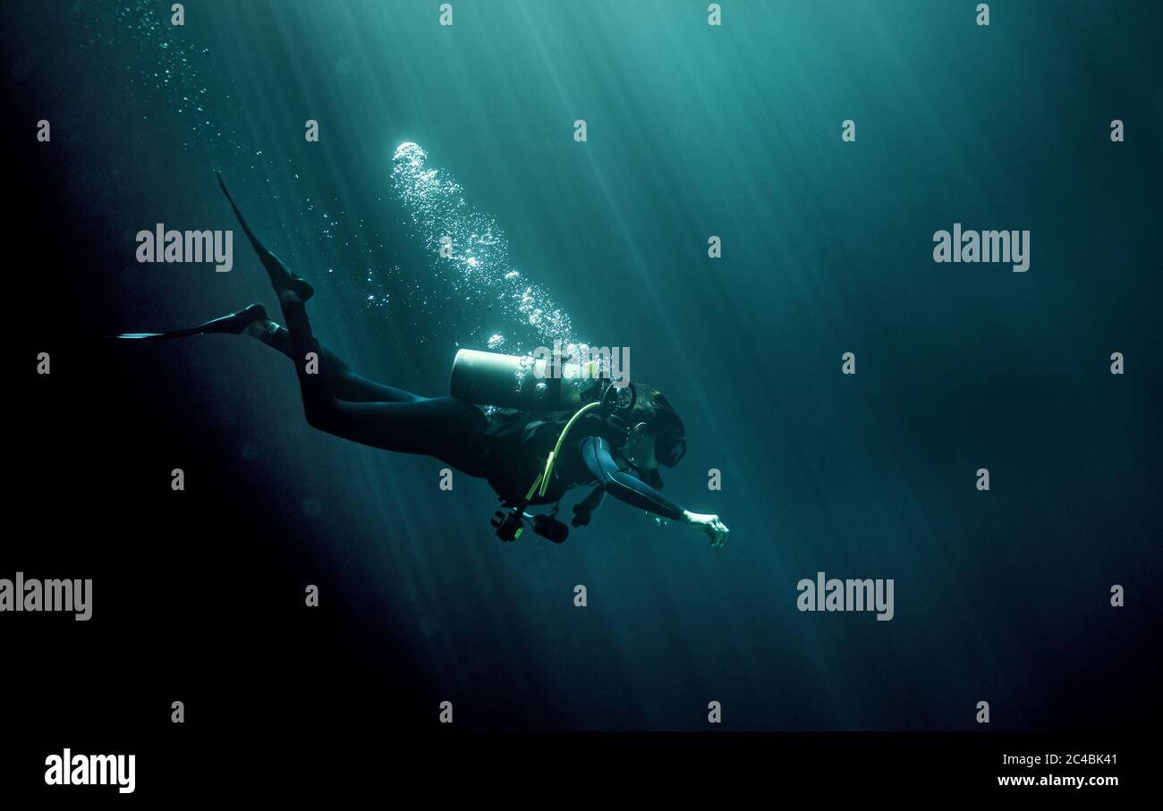 Unterwasseransicht des Tauchers mit Neoprenanzug, Taucherbrille und Sauerstoffflasche, aufsteigende Luftblasen. Stockfoto