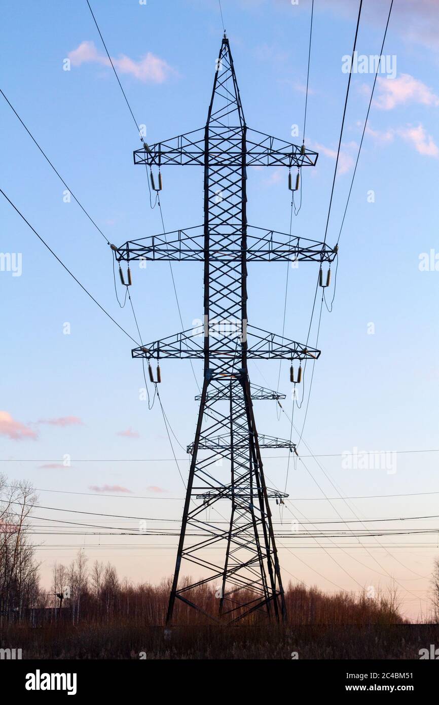 Hochspannungsleitungen in der Mitte eines Feldes bei Sonnenuntergang. Industrialisierung. Elektrifizierung. Stromversorgung. Stockfoto