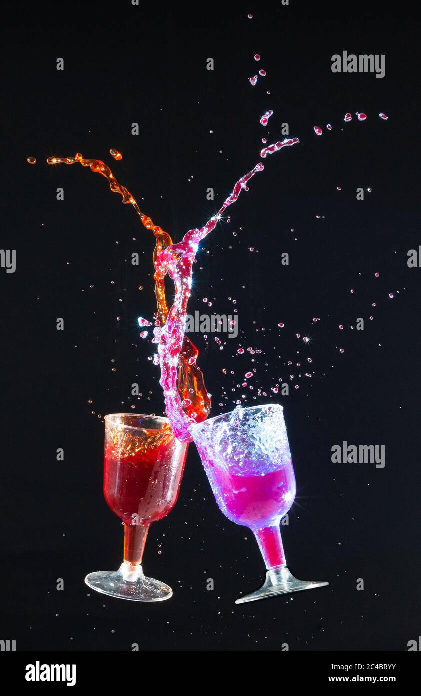 Farbiges Wasser spritzt aus Gläsern in die Luft auf schwarzem Hintergrund Stockfoto