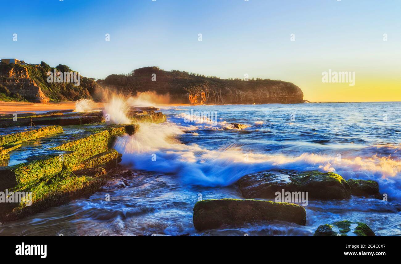 Gefrorene Welle trifft Sandsteinfelsen am Turimetta Strand von Sydney nördlichen Stränden in weichen aufgehenden Sonnenlicht. Stockfoto