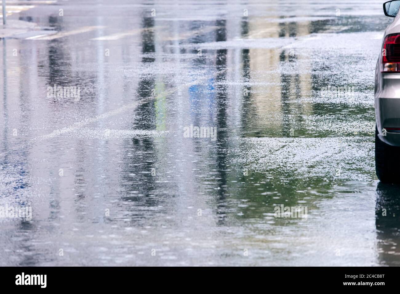 Straße mit Pfützen von Wasser während des Regens und Reflexionen von Stadtgebäuden. Auto auf überfluteten Straße. Regnerisches Wetter in der Stadt. Stockfoto