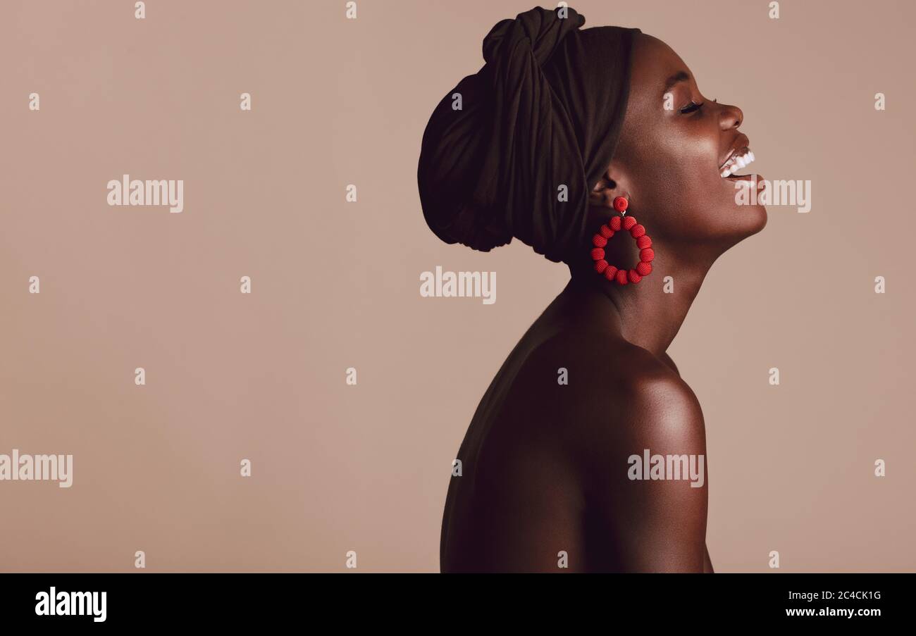 Seitenansicht der modischen afrikanischen Frau lächelt auf beige Hintergrund. Afrikanische Frau mit einem Turban lächelnd im Studio. Stockfoto