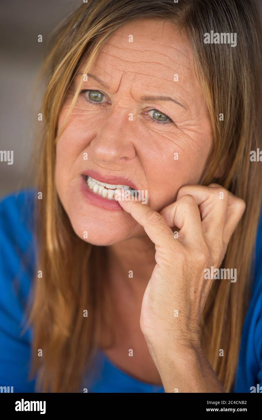 Portrait Attraktive reife Frau mit nervös zögerlich gestressten Gesichtsausdruck, beißende Fingernägel, verschwommener Hintergrund. Stockfoto