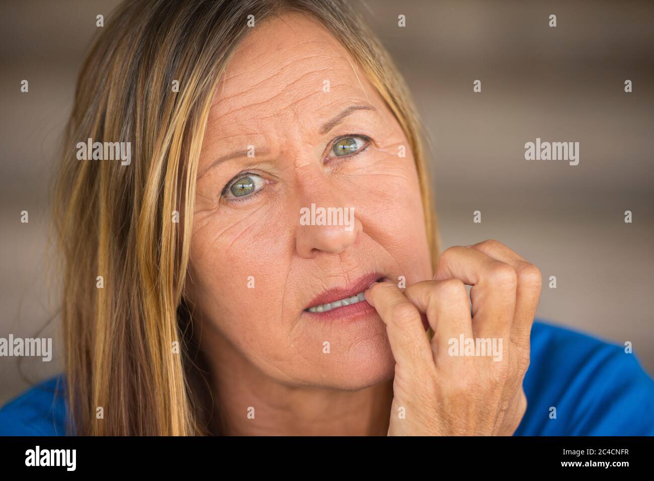 Portrait Attraktive reife Frau mit nervös gestresst unsicheren Gesichtsausdruck, beißende Fingernägel, verschwommener Hintergrund. Stockfoto