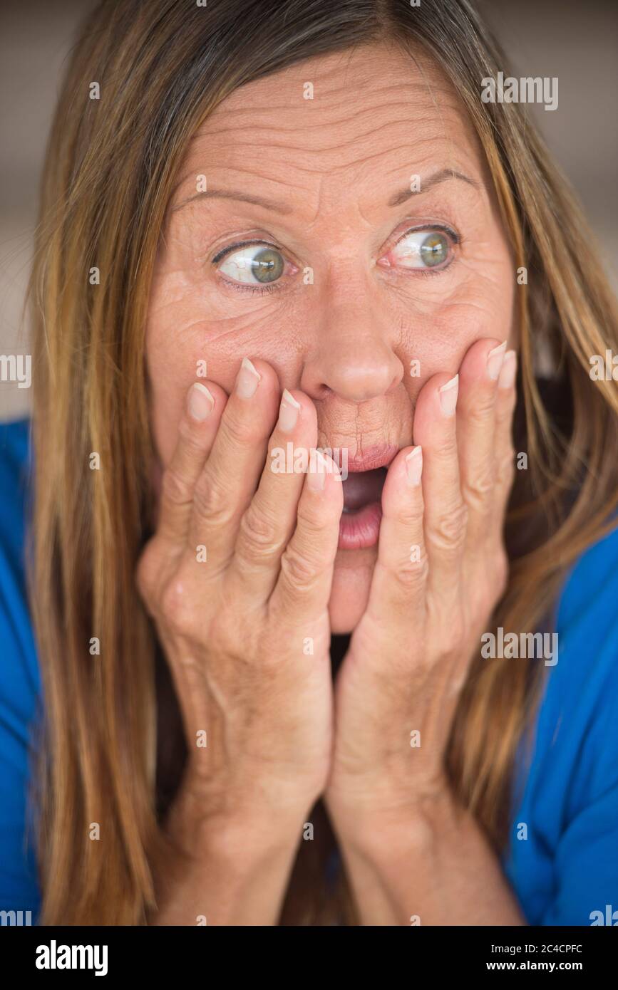 Portrait Attraktive reife Frau mit schockierten, überrascht, ängstlich, erschrocken Ausdruck, den Mund mit der Hand, verschwommener Hintergrund. Stockfoto