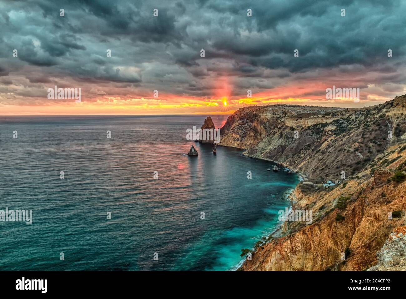 Seascape über dem Strand während des Sonnenuntergangs, mit felsigen Klippen wird durch den warmen Sonnenuntergang beleuchtet. Lange Belichtung. Bewegung verschwommen Wolken. Speicherplatz kopieren. Das Konzept von Stockfoto