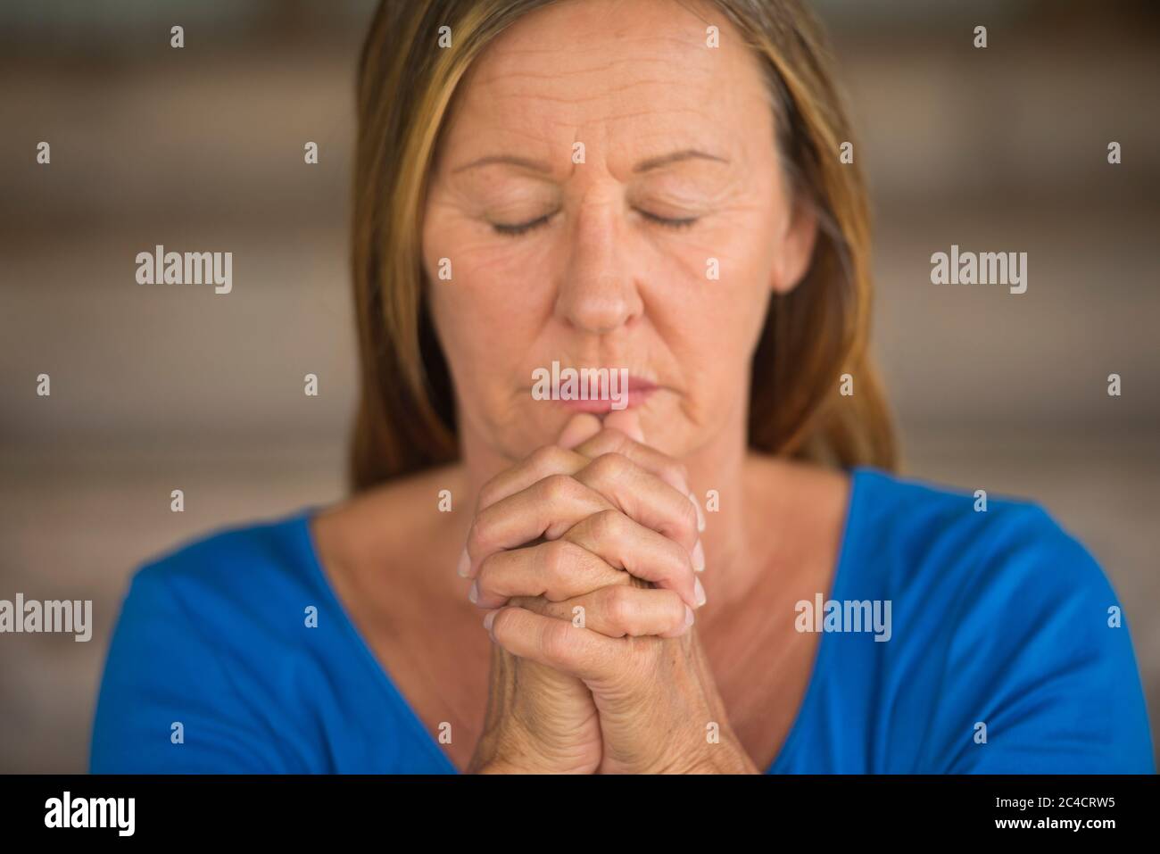 Portrtait Attraktive religiöse ältere Frau beten mit Fokus auf gefaltete Hände, nachdenklich, meditierend, geschlossene Augen, verschwommener Hintergrund. Stockfoto