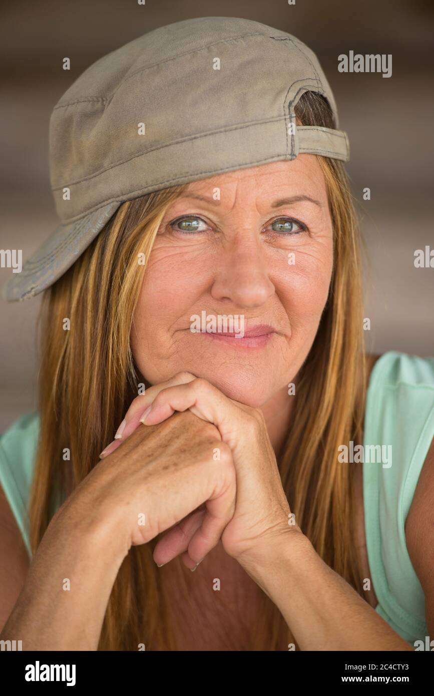 Portrait glücklich attraktive aktive reife Frau trägt grüne sportliche Top und Mütze, freundlich zuversichtlich lächelnden Ausdruck, verschwommener Hintergrund. Stockfoto