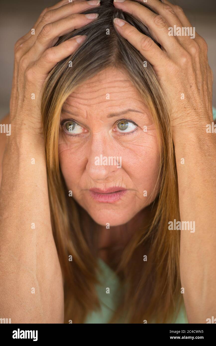 Portrait Attraktive reife Frau, gestresst, ängstlich, verängstigt, unglücklich erschrocken nach oben schauen, Hände über Kopf, verschwommener Hintergrund. Stockfoto