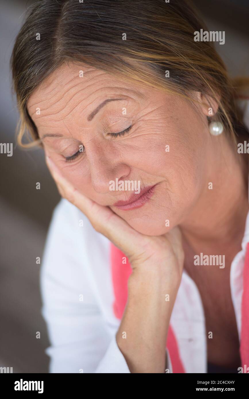 Portrait Attraktive reife Frau müde, geschlossene Augen, abgenutzt, nachdenklich, friedlich mit Kinn auf der Hand, verschwommener Hintergrund. Stockfoto