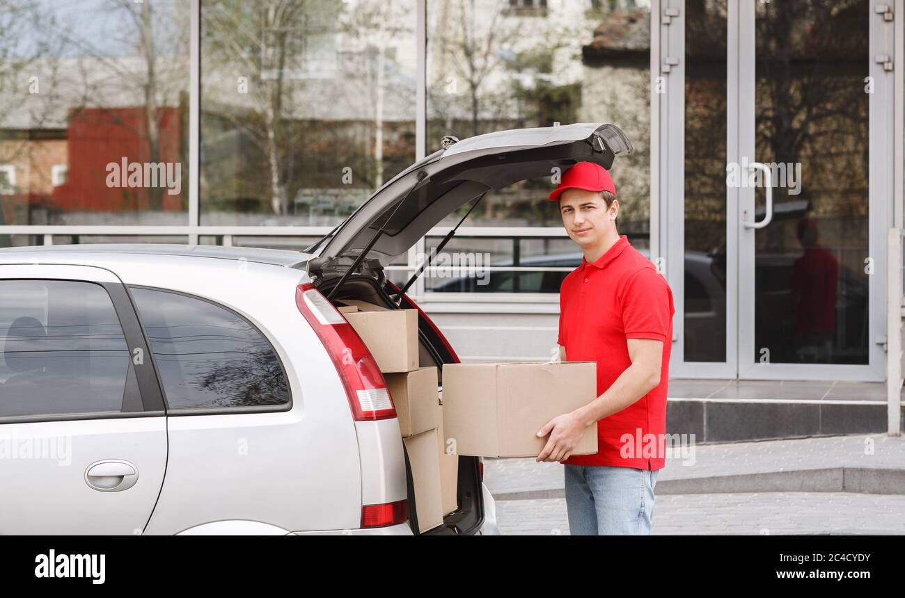 Lieferung mit dem Auto zur Tür. Kurier nimmt großen Kasten vom Stamm Stockfoto