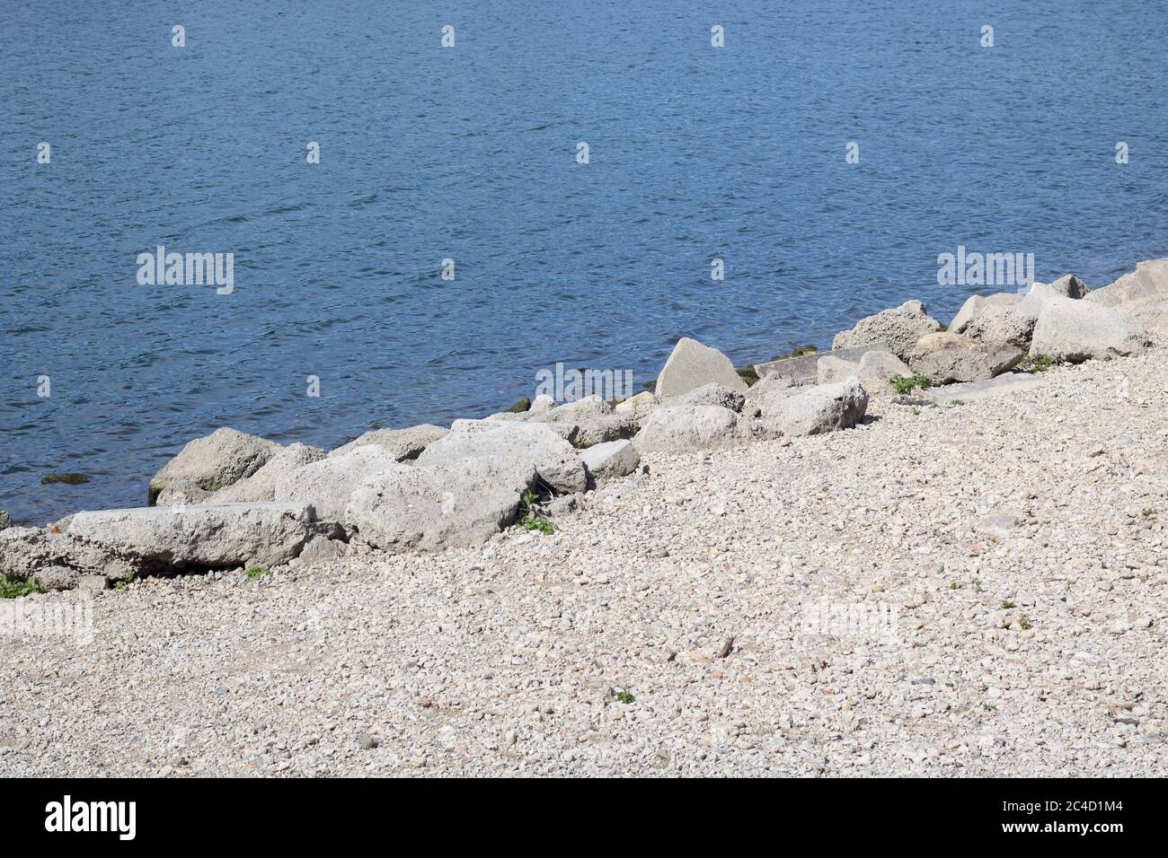 Weißer Kies und Felsen neben blauem, gewelltem Seenwasser mit Kopierraum Stockfoto
