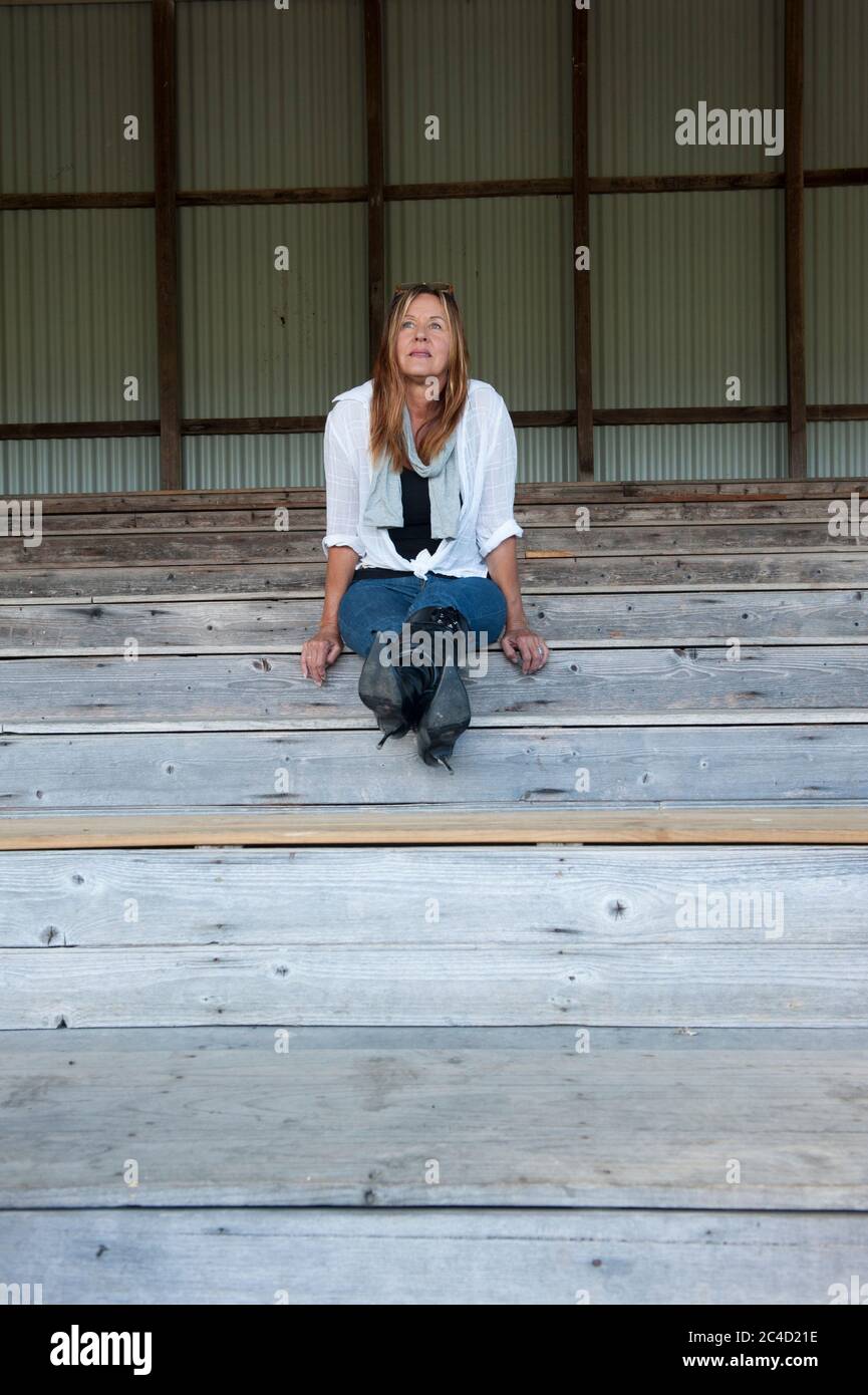 Portrait Attraktive reife Frau sitzt einsam und nachdenklich auf Holztreppe oder Tribüne im Freien, in hohen Fersen Stiletto Stiefel, kopieren Raum. Stockfoto