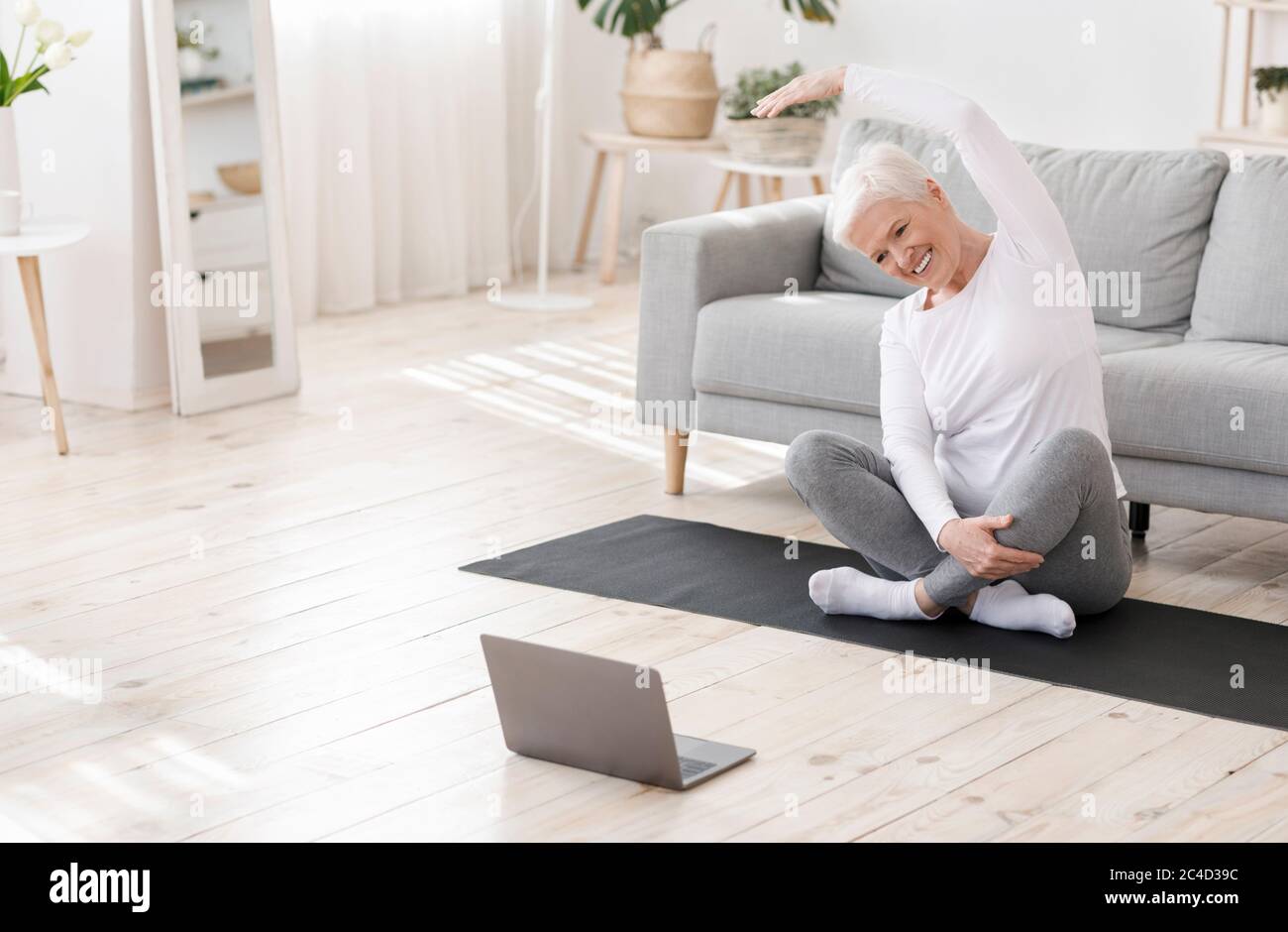 Training Im Inland. Glückliche ältere Frau beim Fitnesstraining vor dem Laptop Stockfoto