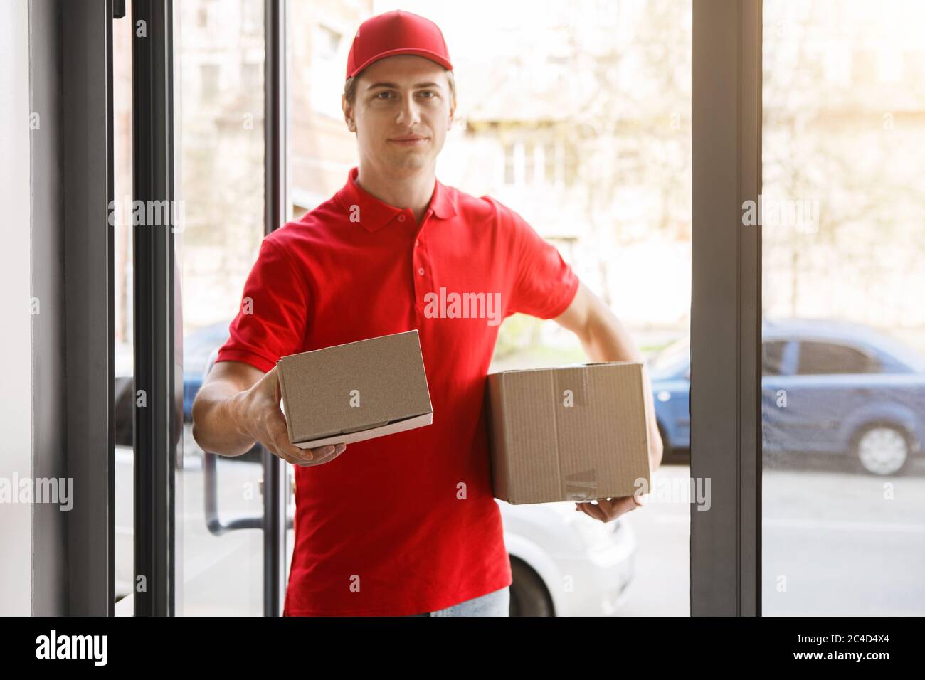 Freundlicher Kurier hält dem Kunden das Paket durch die Schwelle des Hauses aus Stockfoto