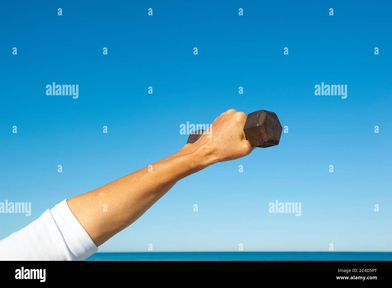 Arm mit Hand um Gewicht gegriffen, isoliert mit blauem Himmel und Ozean als Hintergrund und Kopierraum. Stockfoto
