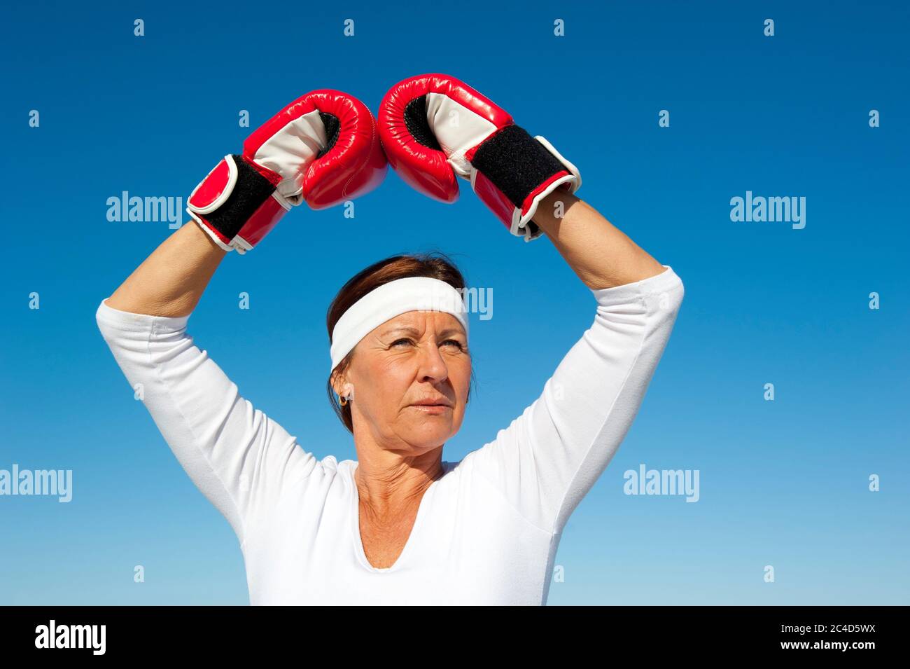 Attraktive aktive ältere Frau mit Boxhandschuhen trainieren, selbstbewusst und fokussiert posieren, isoliert mit blauen Himmel als Hintergrund und Kopierer Raum. Stockfoto