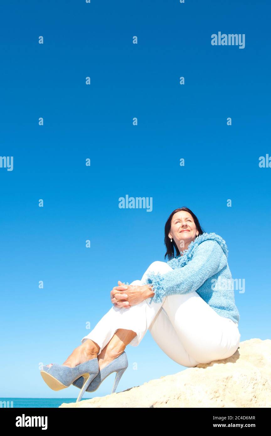 Sexy entspannte Senior Frau in High Heel Schuhe genießen aktiven Ruhestand, Urlaub auf See, mit Meer und blauen Himmel als Hintergrund und Kopierer Raum. Stockfoto