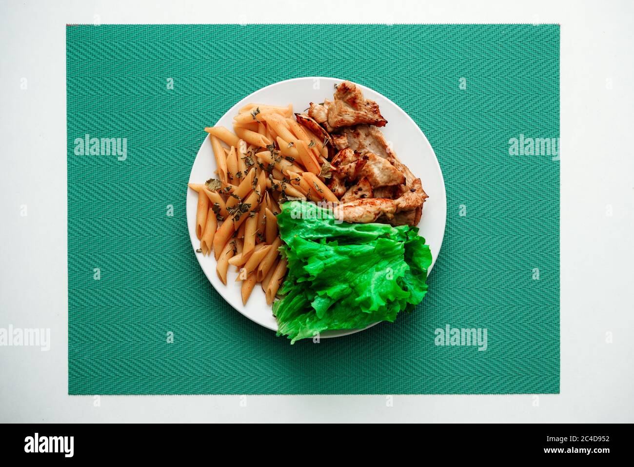 Teller mit gekochter Penne-Pasta, gebratenem Huhn und Salat auf türkisfarbenem Stoff Stockfoto