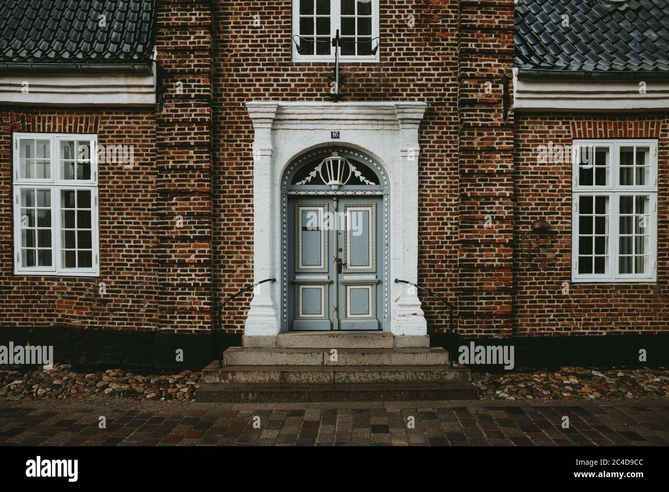 Die Vorderansicht eines alten Backsteinhauses mit weißen Fenstern und Eingang mit hellblauen Türen in der ältesten dänischen Stadt Ribe während des Herbstregentages Stockfoto