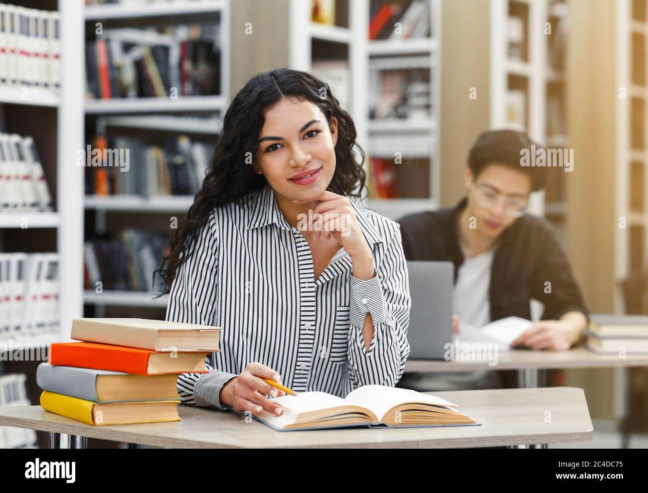 Fröhliches lateinisches Mädchen, das an der Rezeption in der Bibliothek sitzt Stockfoto