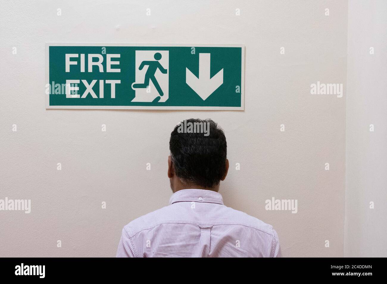 Mann sah, wie er in eine feste Wand ging, unter einem Schild mit dem Feuerausgang in einem Bürokomplex. Der eigentliche Feuerausgang ist die Treppe hinunter. Stockfoto