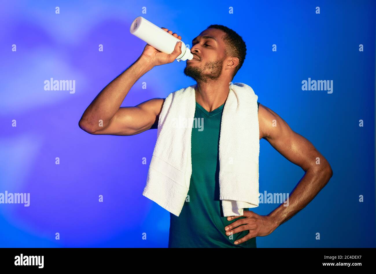 Black Fitness Guy Trinkwasser Auf Blauem Hintergrund, Studio Stockfoto