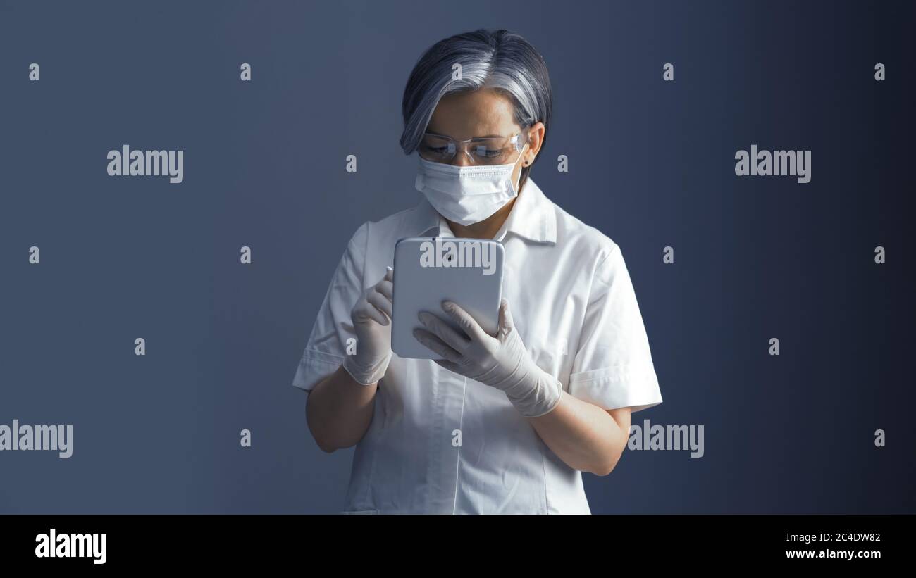 Ärztin arbeitet mit Datenbank auf digitalen Tablet. Grauhaarige Frau in medizinischen Uniform arbeitet mit elektronischen Gadget Stockfoto